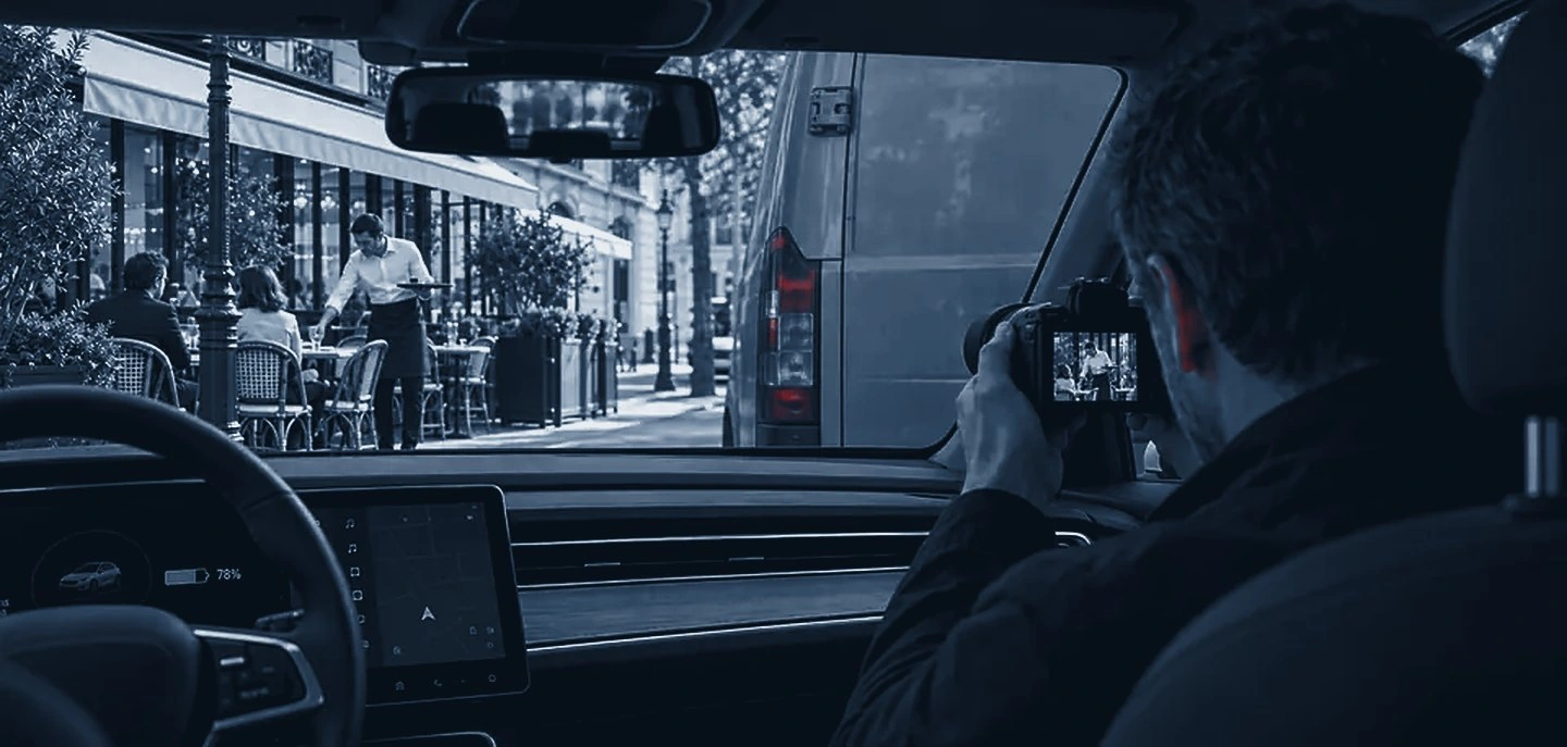 Détective dans une voiture photographiant une activité professionnelle en terrasse de restaurant, scène illustrative.
